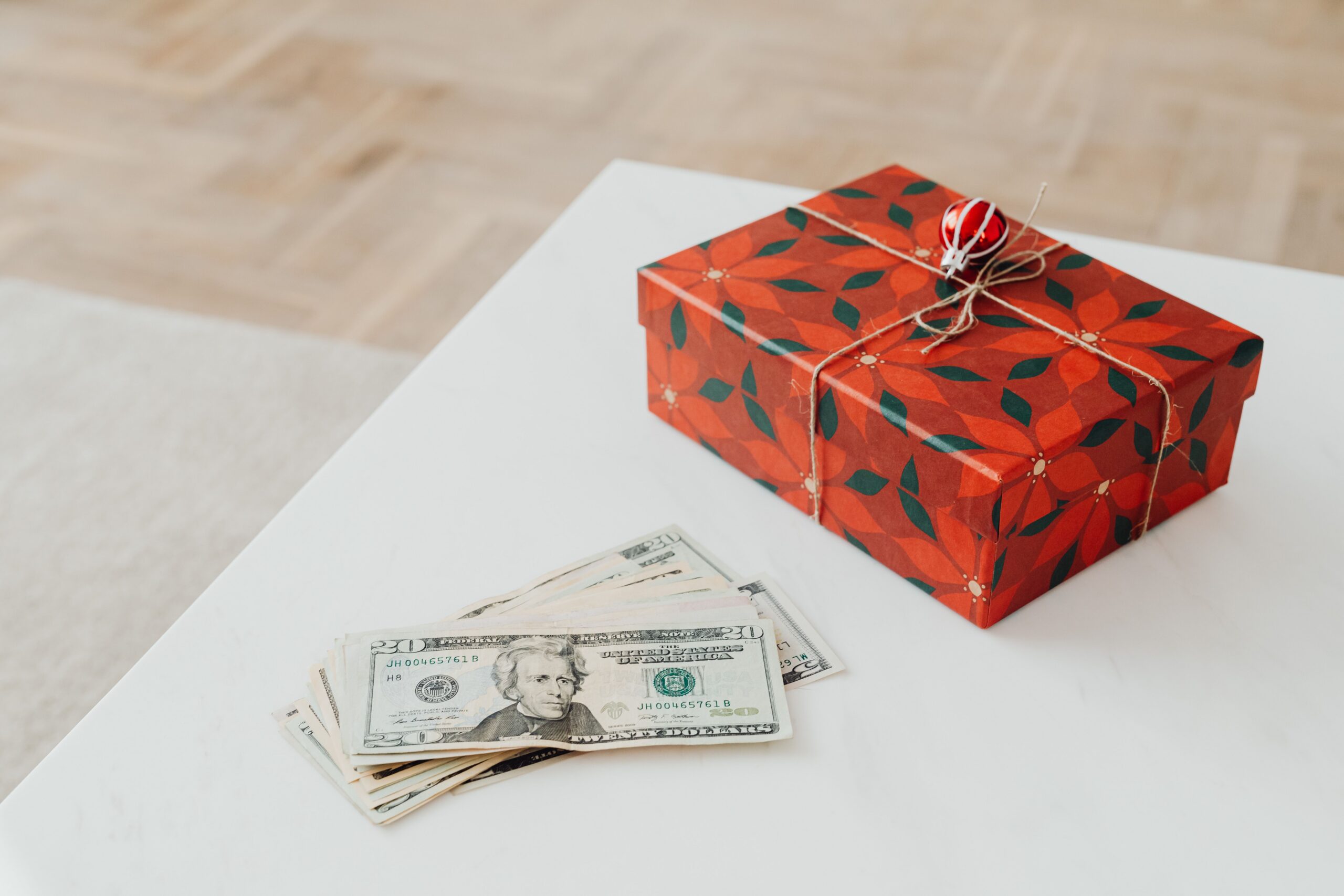 A holiday-themed gift box with US dollar bills on a white table indoors.