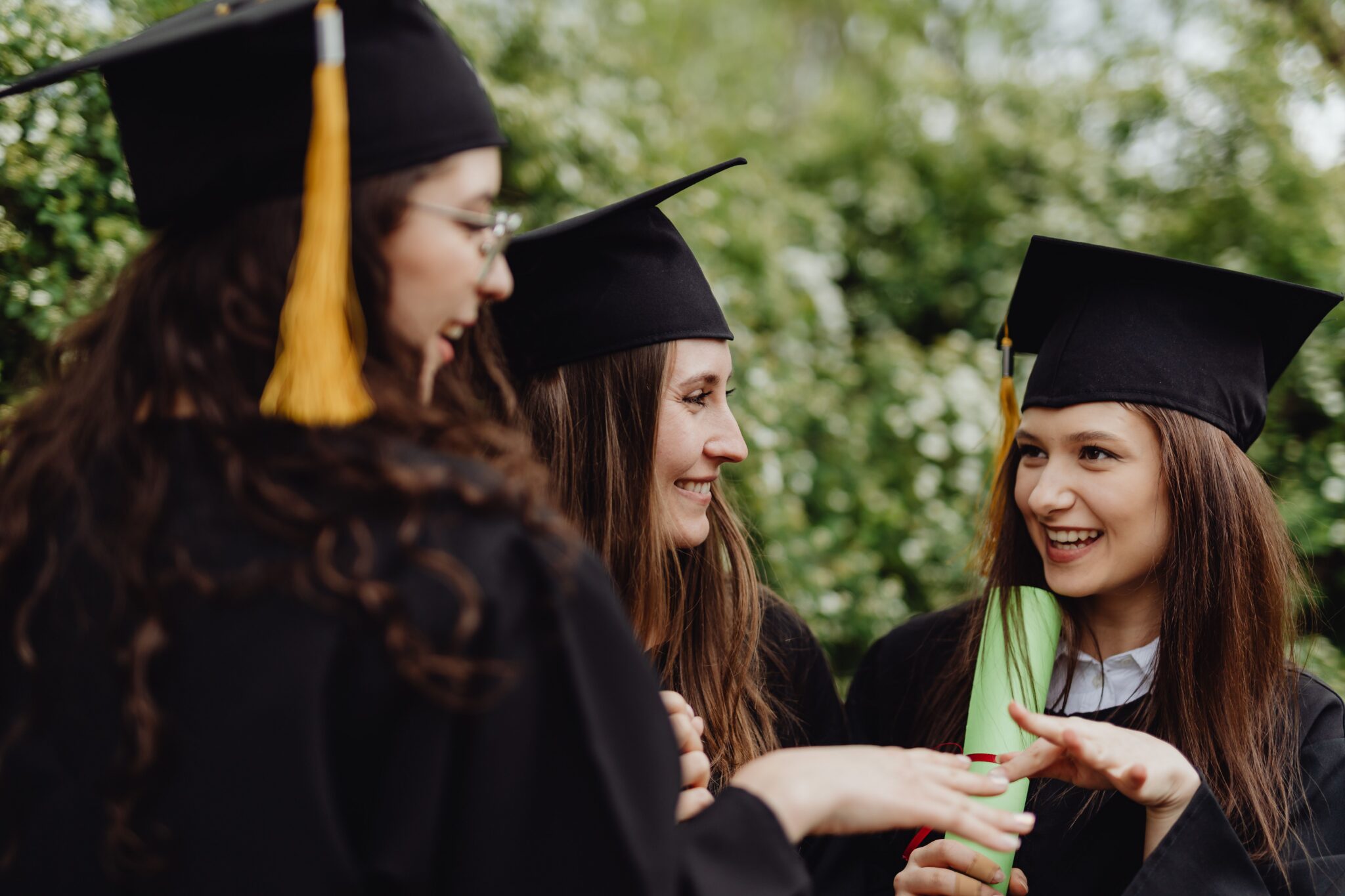 Three young women in caps and gowns celebrating graduation outdoors.